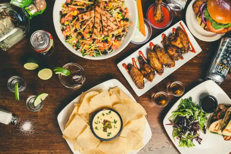 A table of shared dishes — salads, grilled skewers, dips and drinks — seen from above